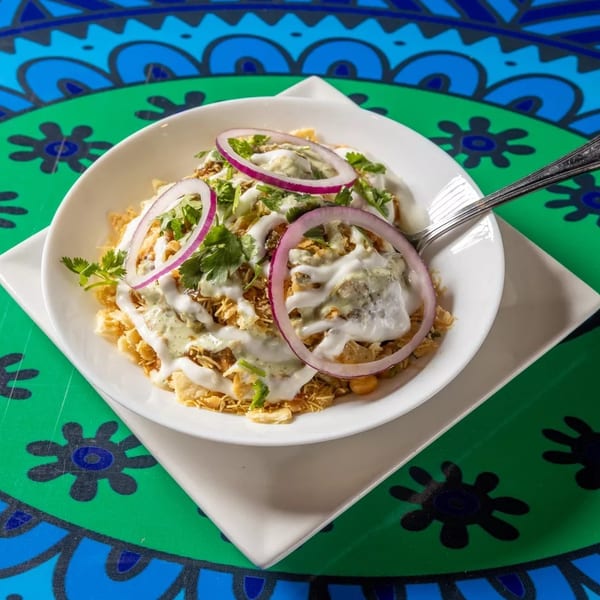A bowl of Indian chaat with yogurt, red onions, and cilantro on a colorful table.