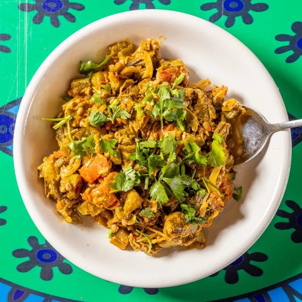A white bowl filled with a vibrant okra and tomato curry, garnished with fresh cilantro.