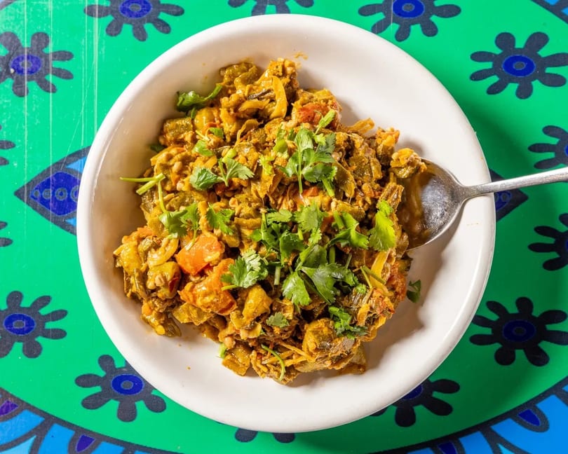 A white bowl filled with a vibrant okra and tomato curry, garnished with fresh cilantro.