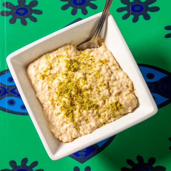 Creamy rice pudding topped with green pistachios in a white bowl on a vibrant green patterned tablecloth.