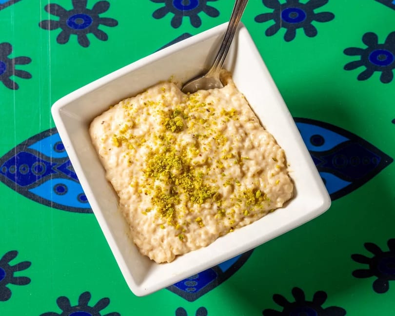 Creamy rice pudding topped with green pistachios in a white bowl on a vibrant green patterned tablecloth.