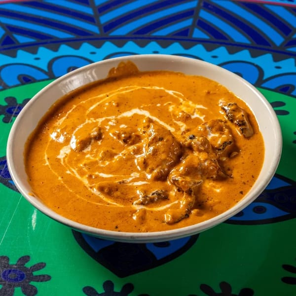 A bowl of creamy orange butter chicken with white swirls, on a colorful patterned placemat.