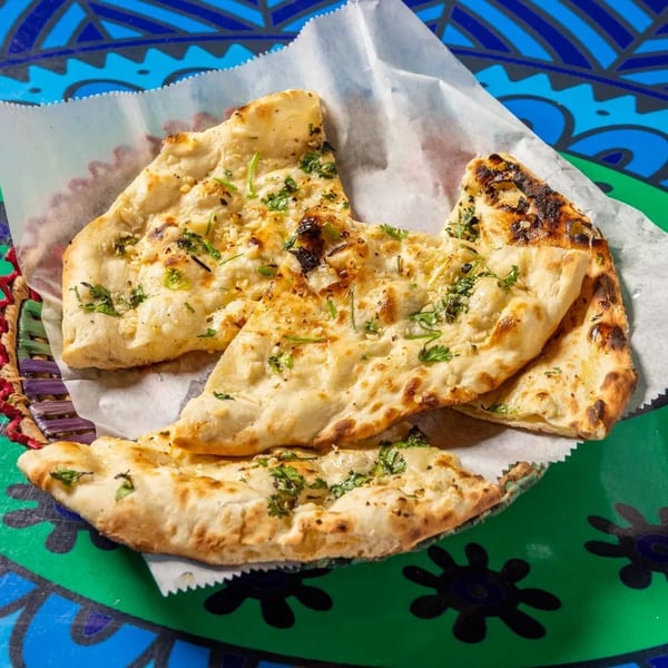 Garlic naan bread pieces with cilantro in a basket on a colorful patterned table.