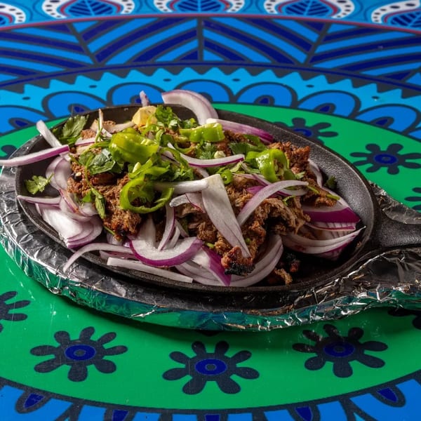Sizzling meat with red onions, green peppers, and cilantro in a cast iron pan.