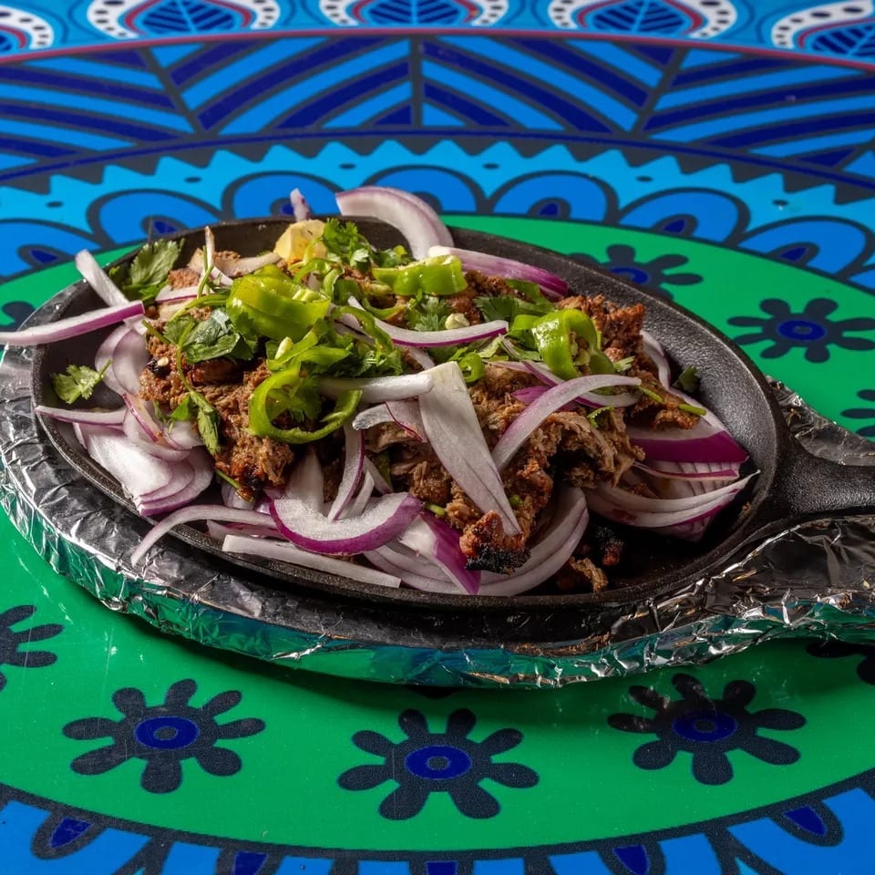 Sizzling meat with red onions, green peppers, and cilantro in a cast iron pan.