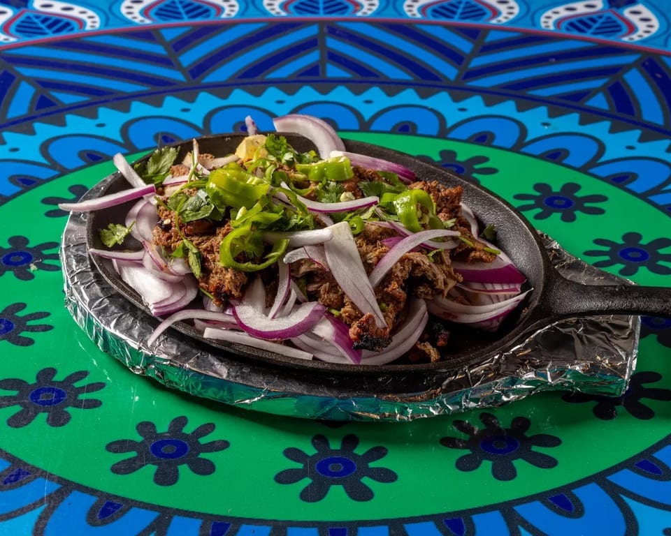 Sizzling meat with red onions, green peppers, and cilantro in a cast iron pan.