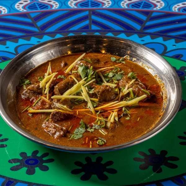 A metal bowl of rich, brown curry with meat, garnished with fresh ginger and cilantro.