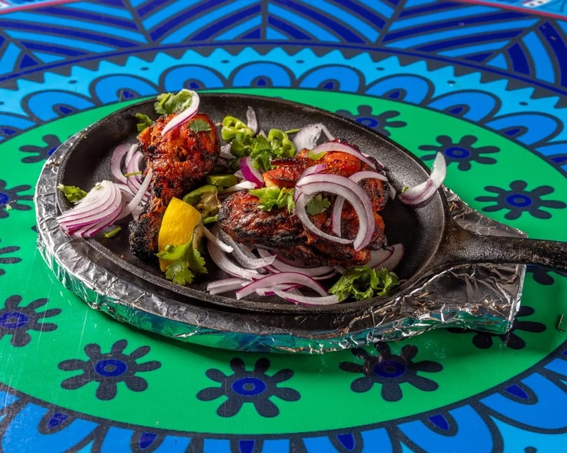 Tandoori chicken with red onions, green peppers, and lemon in a cast iron skillet.
