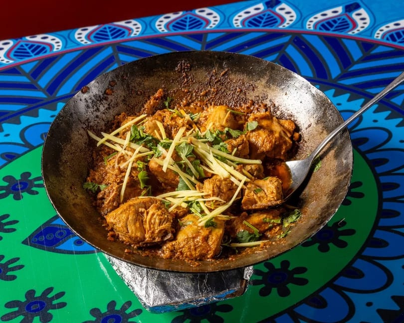 Chicken karahi with ginger and cilantro in a metal wok on a colorful patterned table.