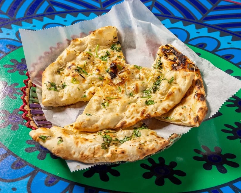 Garlic naan bread pieces with cilantro in a basket on a colorful patterned table.